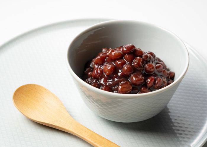 A bowl of Japanese red beans on a white serving tray, next to a wooden spoon.